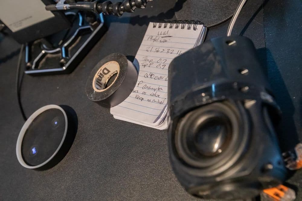 Foto: Werkzeuge und Bauteile auf einem schwarzen Tisch, darunter Isolierband, eine Linse und Elektronikkomponenten.